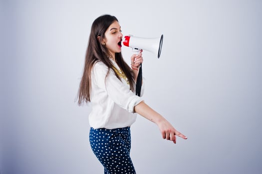 Portrait of a young woman in blue trousers and white blouse posing with megaphone in the studio. photo