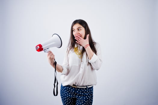Portrait of a young woman in blue trousers and white blouse posing with megaphone in the studio. photo