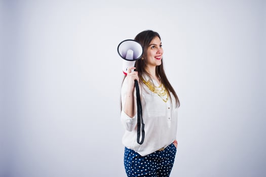 Portrait of a young woman in blue trousers and white blouse posing with megaphone in the studio. photo