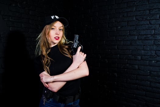 FBI female agent in cap and with gun at studio against dark brick wall. photo