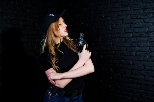FBI female agent in cap and with gun at studio against dark brick wall. photo
