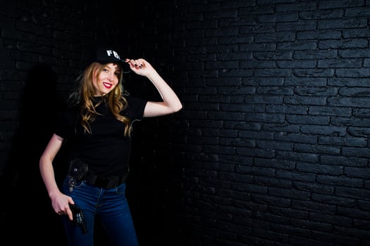 FBI female agent in cap and with gun at studio against dark brick wall. photo
