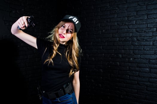 FBI female agent in cap and with gun at studio against dark brick wall. photo