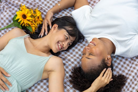 Couple of lesbian people having picnic in the park during summer while having romantic time and lying down on the lawn to promote pride month and marriage equality photo