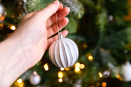 Woman hand decorating Christmas tree. Christmas tree with wite and silver decorations, ornaments toy and ball. Modern classical style interior design. Christmas eve at home, time for celebration. photo