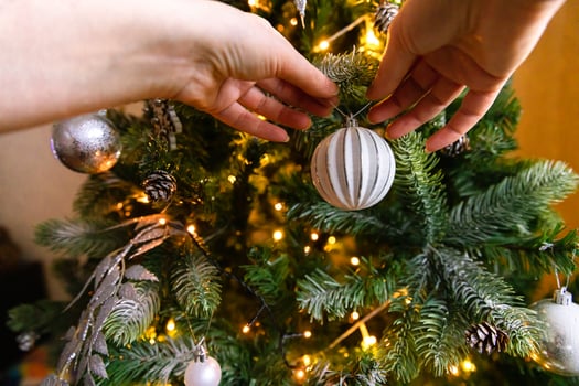 Woman hands decorating Christmas tree. Christmas tree with wite and silver decorations, ornaments toy and ball. Modern classical style interior design. Christmas eve at home, time for celebration. photo