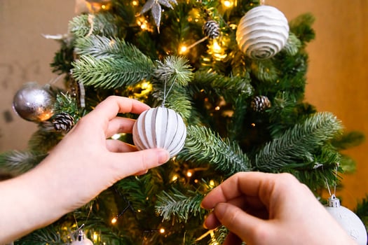 Woman hands decorating Christmas tree. Christmas tree with wite and silver decorations, ornaments toy and ball. Modern classical style interior design. Christmas eve at home, time for celebration. photo