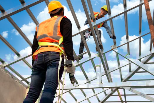 Construction workers wear safety straps while working on the building's roof structure at a construction site. Roofer using a pneumatic nail gun. photo