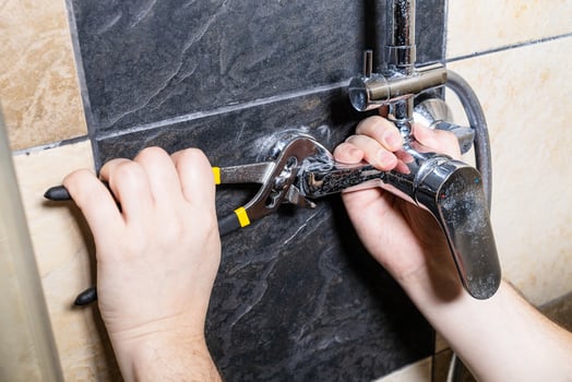 plumber unscrews shower faucet on tiled wall photo