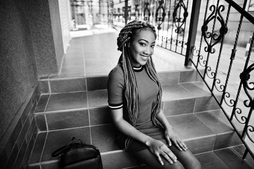 Cute and slim african american girl in red dress with dreadlocks and backpack posed outdoor, sitting on stairs. Stylish black model. photo