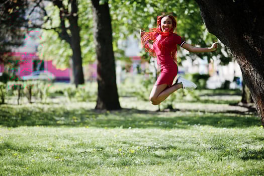 Cute and slim african american girl in red dress with dreadlocks jump outdoor in spring park. Stylish black model. photo