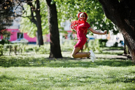 Cute and slim african american girl in red dress with dreadlocks jump outdoor in spring park. Stylish black model. photo