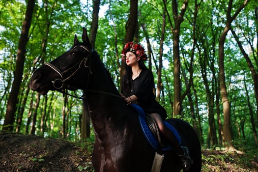 Mystical girl in wreath wear in black at horse in wood. photo