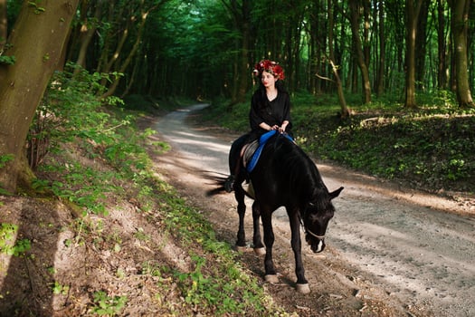 Mystical girl in wreath wear in black at horse in wood. photo