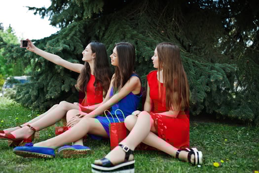 Three teenagers girl in blue and red dresses posed outdoor and making selfie at mobile phone. photo