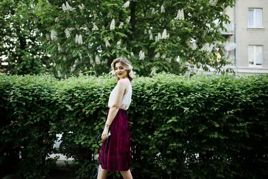 Fashionable and beautiful blonde model girl in stylish red velvet velour skirt, white blouse, posed at park with phone and earphones. photo