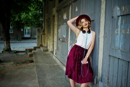 Fashionable and beautiful blonde model girl in stylish red velvet velour skirt, white blouse and hat, posed with phone and earphones. photo