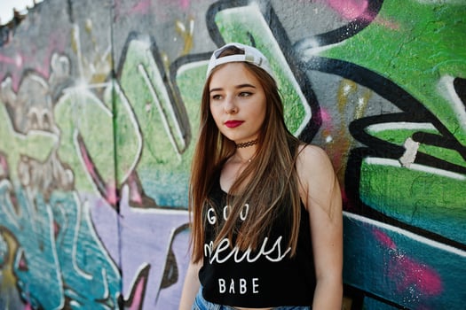 Stylish casual hipster girl in cap  and jeans wear against large graffiti wall. photo