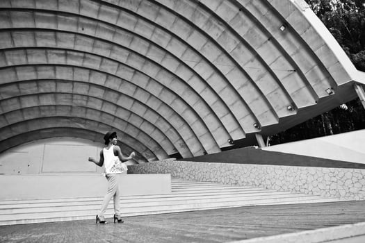 Amazing african american model woman in green pants and black hat posed outdoor against arena hall. photo