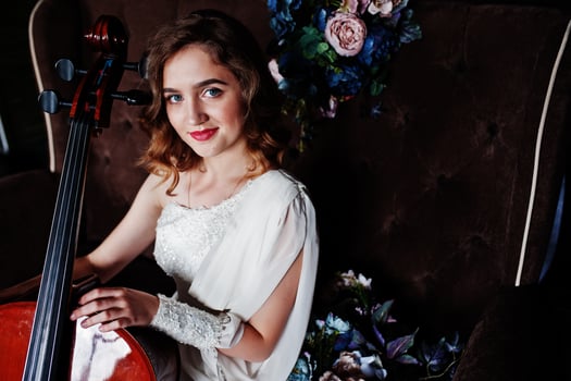 Pretty young gilrl musician in white dress with double bass sitting on brown vintage sofa. photo