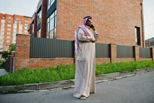 Middle Eastern arab business man posed on street against modern building with sunglasses, speaking on mobile phone. photo