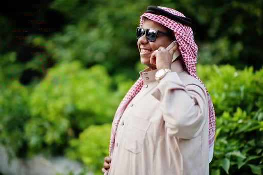 Middle Eastern arab business man posed on street with sunglasses, speaking on mobile phone. photo