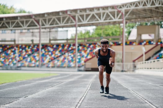 African american male athlete in sportswear racing alone down a running track at stadium. photo