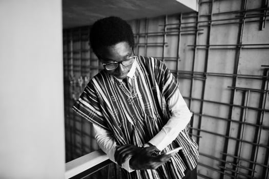 African businessman in traditional clothes and glasses with mobile phone at hand posed at modern building indoor. photo