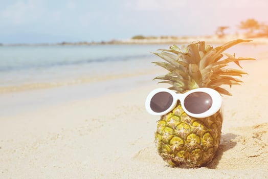 pineapples wearing stylish mirrored sunglasses on the sand against turquoise sea. Tropical idea summer vacation on the beach concept. filter vintage photo