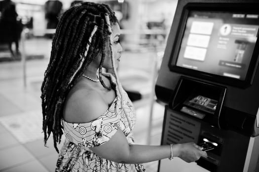 Cute small height african american girl with dreadlocks, wear at coloured yellow dress, against ATM with credit card at hand. Black and white. photo