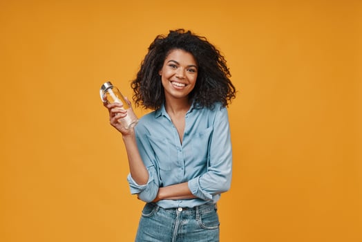 Beautiful young African woman in casual clothing looking at camera and holding bottle photo