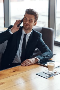 Handsome young businessman in full suit talking on the smart phone while sitting in the restaurant photo
