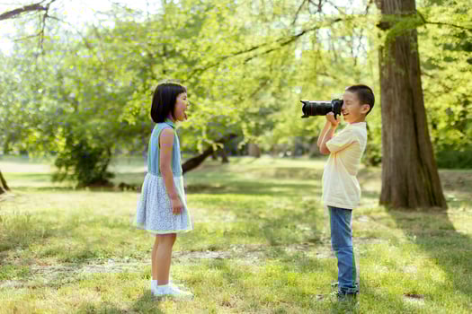 Little asian boy acting like a professional photographer while taking photos of his little sister