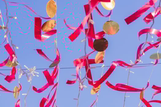 red festive ribbons and gold circles against blue sky. Colorful garland for event decoration photo
