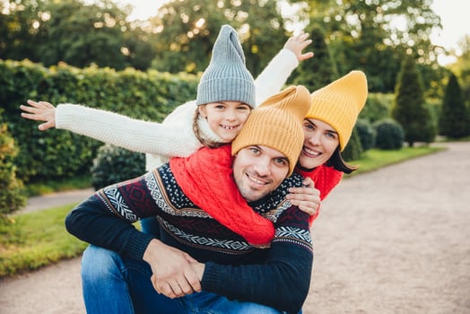 Having nice time together Smiling excited woman, man and their little female child, wear warm knitted clothes, embrace each other, walk in park, being in good mood. Family give support, encouragement photo