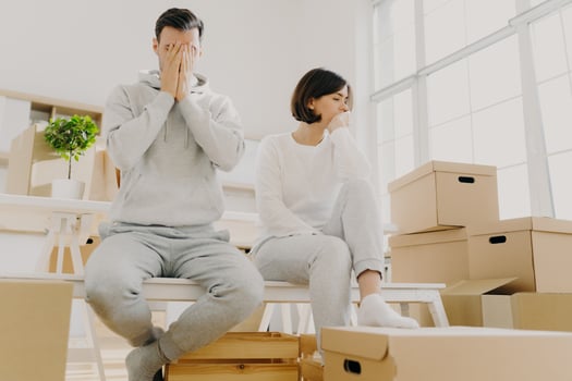 Worried couple pose near stack of cardboard boxes, have to move in other flat, have no money for rent, have dejected sad expressions, sit together in white room, have family conflict and divorce photo