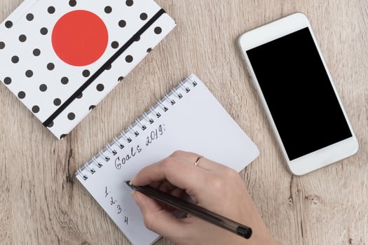 young woman hands hold opened notebook pages with black pen on  wooden table. Goals 2019 list. photo