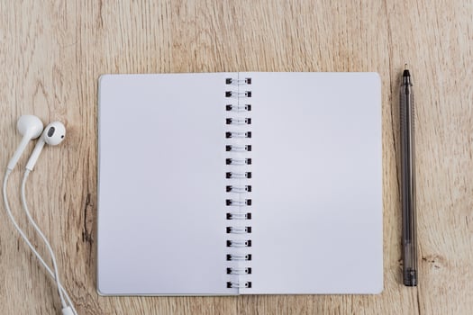 Business and office concept - blank notebook, headphones and black pen on wooden table. Minimal flat lay, top view. photo