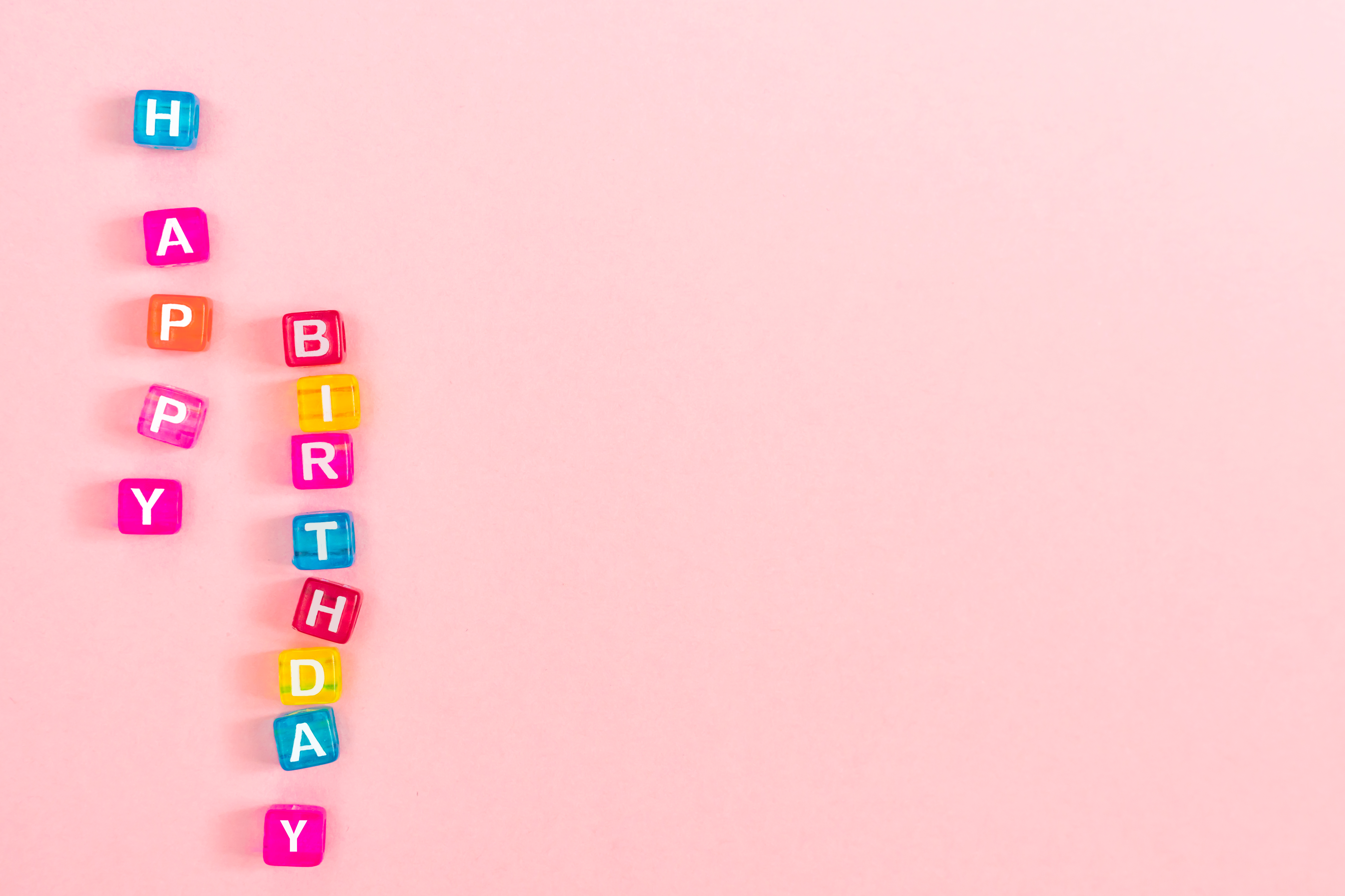 Happy birthday inscription made of colorful cube beads with letters. Festive pink background concept with copy space photo