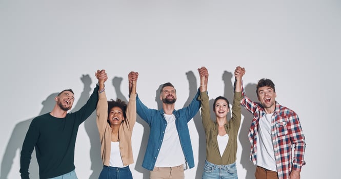 Group of cheerful young people in casual clothing holding hands clasped and looking up photo