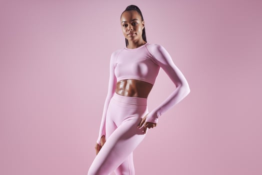 Attractive young African woman in sports clothing standing against pink background photo