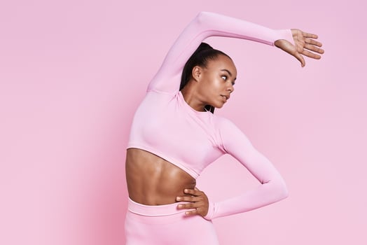 Attractive young African woman doing stretching exercises against pink background photo
