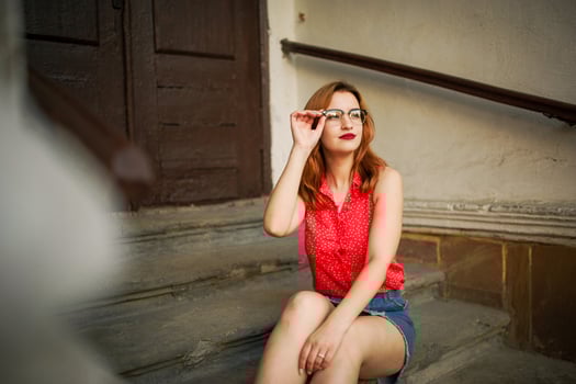 Attractive redhaired woman in eyeglasses, wear on red blouse and jeans skirt posing. photo