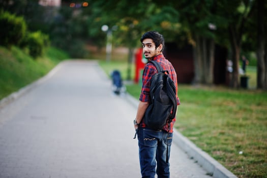 Young indian student man at red checkered shirt and jeans with backpack posed at street. photo
