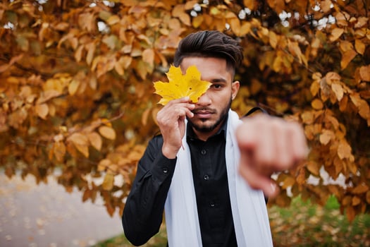 Indian stylish man in black traditional clothes with white scarf posed outdoor against yellow autumn and show finger. photo