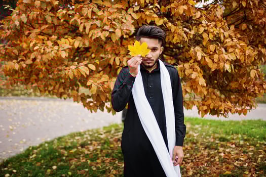 Indian stylish man in black traditional clothes with white scarf posed outdoor against yellow autumn. photo