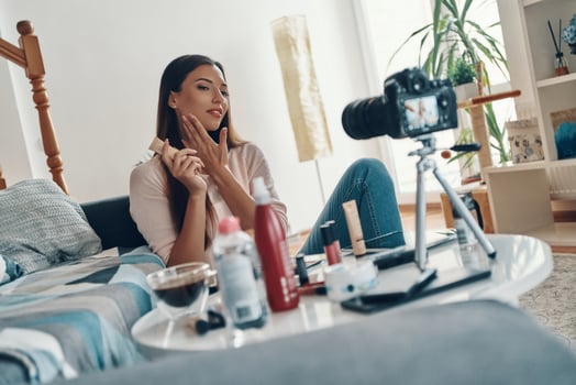 Beautiful young woman applying beauty product and smiling while making social media video photo