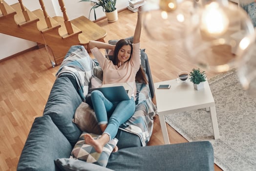 Top view of beautiful young woman in casual clothing using laptop and smiling while spending time at home photo