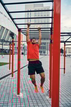 Full length of handsome young man in sports clothing doing pull ups while exercising outdoors on the city street photo