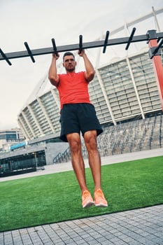 Full length of motivated young man in sports clothing doing pull ups while exercising outdoors on the city street photo